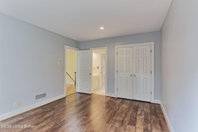 unfurnished bedroom with dark wood-style floors, a closet, visible vents, ensuite bathroom, and baseboards