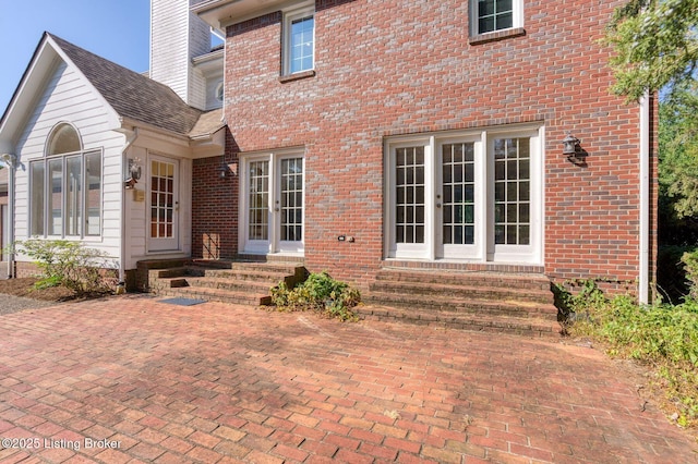 rear view of house featuring entry steps, french doors, a chimney, and brick siding