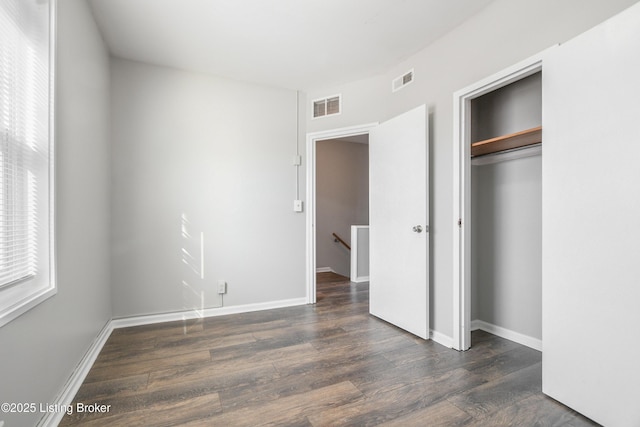 unfurnished bedroom with a closet, wood finished floors, visible vents, and baseboards