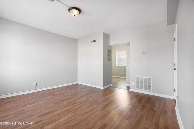 spare room featuring electric panel, visible vents, baseboards, and wood finished floors