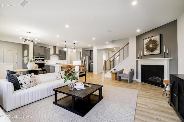 living area featuring recessed lighting, a fireplace, visible vents, stairs, and light wood finished floors