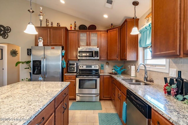 kitchen with arched walkways, brown cabinetry, appliances with stainless steel finishes, vaulted ceiling, and a sink