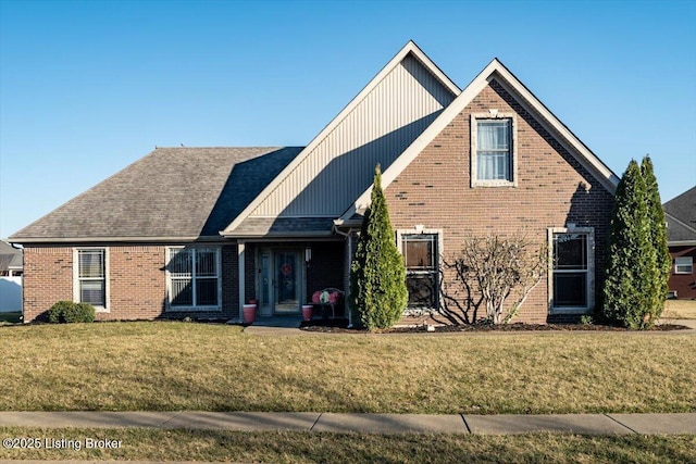 view of front of home with a front yard, brick siding, and roof with shingles