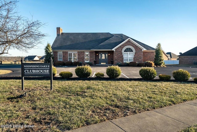 ranch-style house with a front yard, a chimney, and brick siding