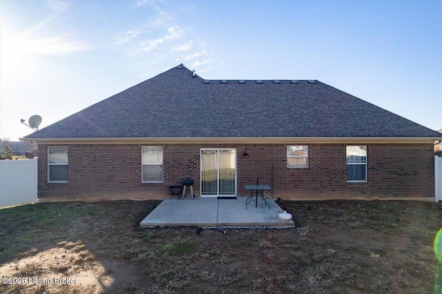 rear view of property with a shingled roof, a patio area, fence, and brick siding