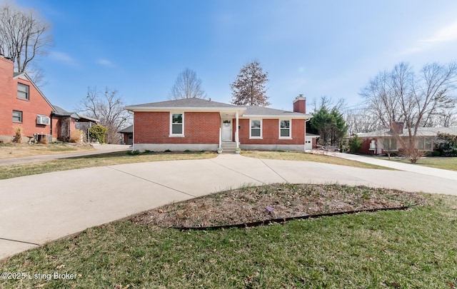 view of front of house with brick siding, concrete driveway, a chimney, and a front lawn