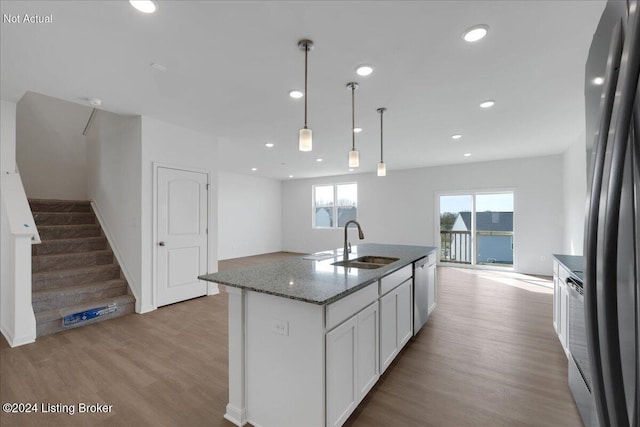 kitchen with hanging light fixtures, light wood-style floors, white cabinets, a sink, and dark stone counters