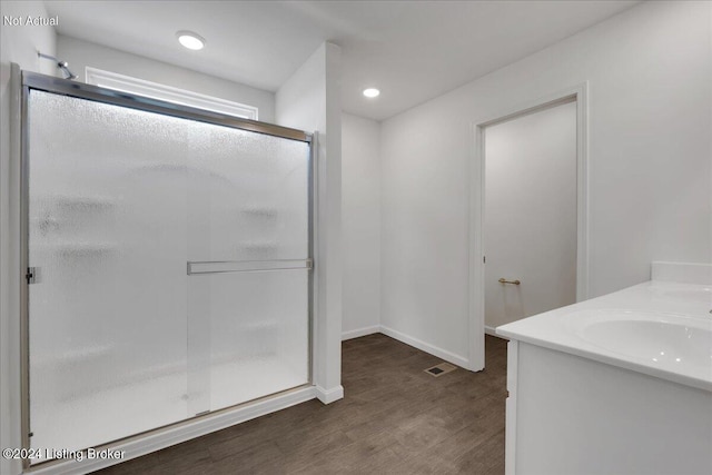 bathroom featuring a sink, wood finished floors, visible vents, baseboards, and a stall shower