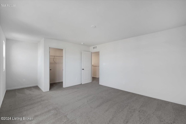 unfurnished bedroom with a spacious closet, a closet, carpet, and visible vents