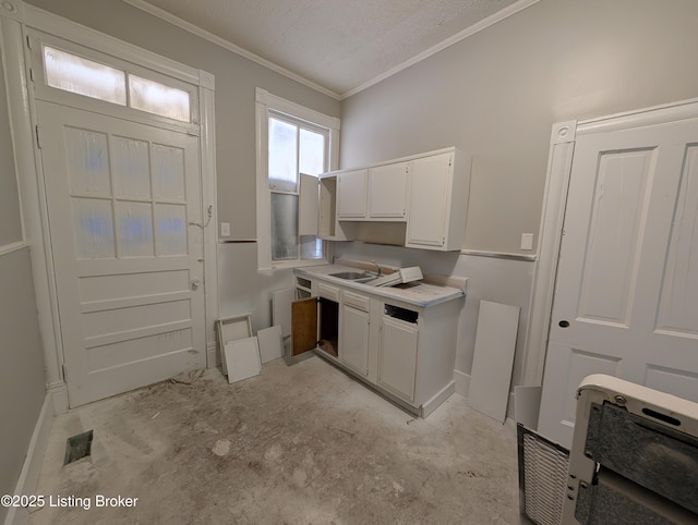 kitchen featuring a textured ceiling, a sink, white cabinets, light countertops, and ornamental molding