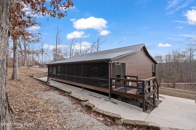 back of house with driveway, a sunroom, and metal roof