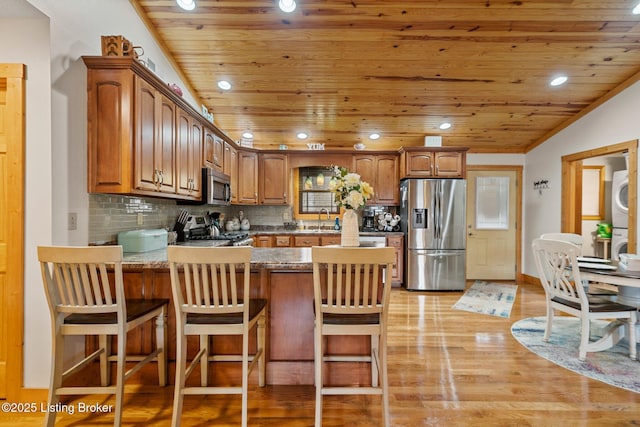 kitchen with a peninsula, stacked washing maching and dryer, wood ceiling, and appliances with stainless steel finishes