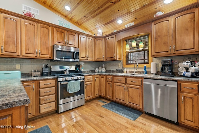 kitchen featuring lofted ceiling, stainless steel appliances, a sink, visible vents, and brown cabinetry