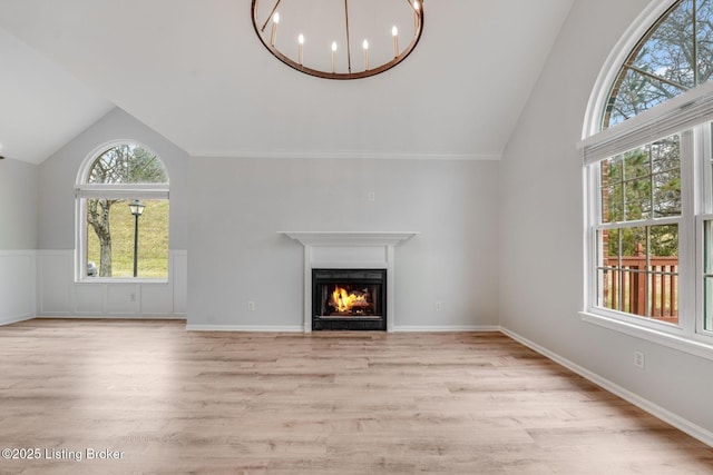 unfurnished living room with a chandelier, a warm lit fireplace, vaulted ceiling, and light wood finished floors