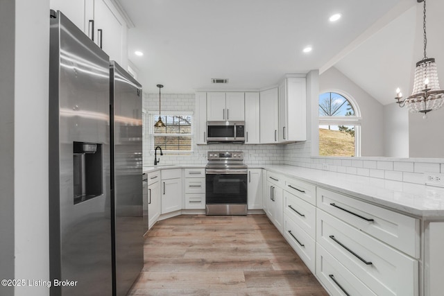 kitchen with visible vents, light wood-style flooring, appliances with stainless steel finishes, a peninsula, and backsplash