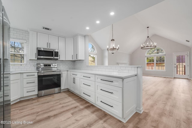 kitchen featuring visible vents, decorative backsplash, a peninsula, stainless steel appliances, and light countertops