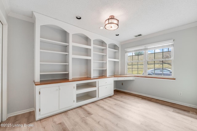 unfurnished office featuring a textured ceiling, built in desk, light wood finished floors, and visible vents