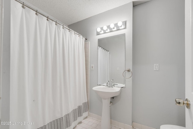 full bath with a textured ceiling, curtained shower, tile patterned flooring, toilet, and baseboards