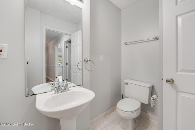 bathroom featuring baseboards, toilet, tile patterned flooring, a textured ceiling, and a sink