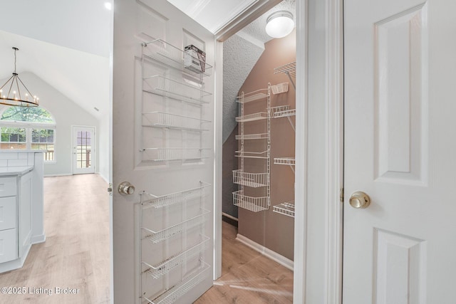 spacious closet featuring vaulted ceiling, light wood-style flooring, and an inviting chandelier