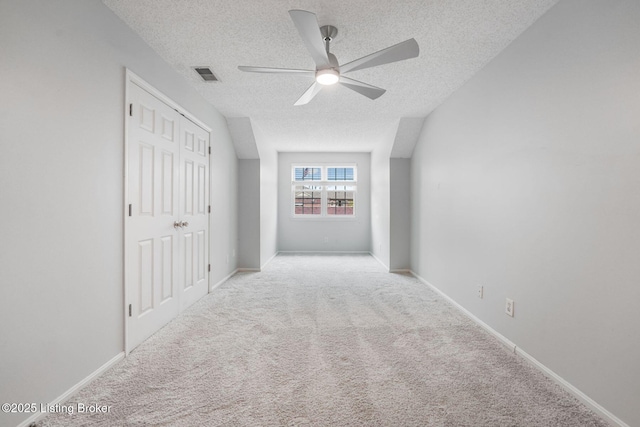 carpeted empty room featuring a textured ceiling, a ceiling fan, visible vents, and baseboards