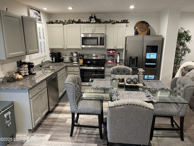 kitchen with stainless steel appliances, recessed lighting, light wood-style floors, a sink, and light stone countertops