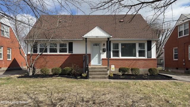 view of front facade with a shingled roof, a front yard, and brick siding