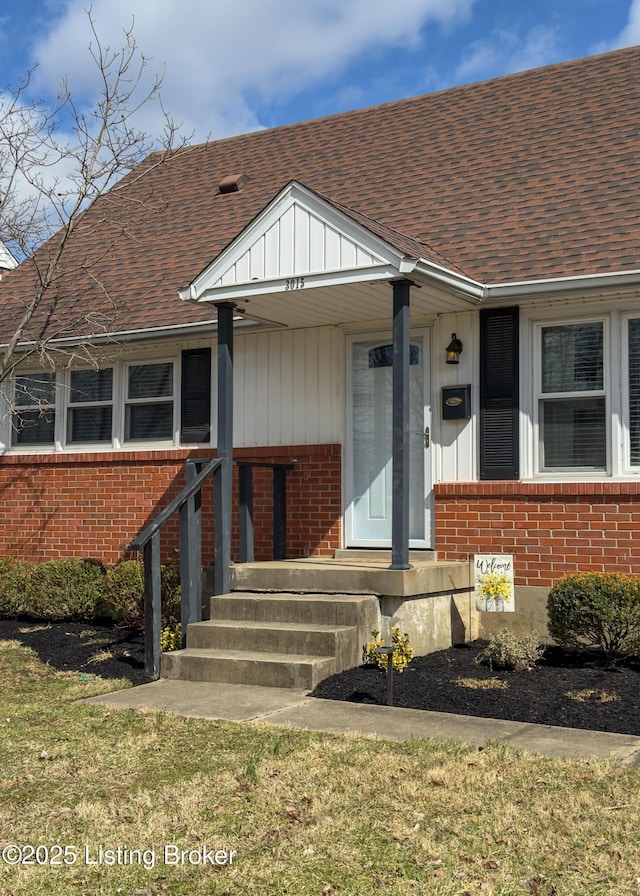 doorway to property with brick siding and a shingled roof