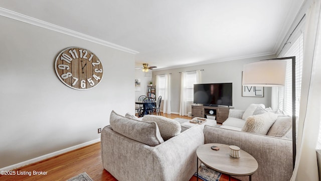 living area with a ceiling fan, crown molding, baseboards, and wood finished floors