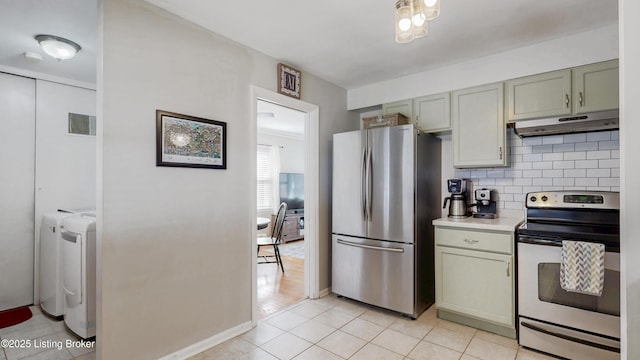 kitchen with washing machine and clothes dryer, tasteful backsplash, light countertops, appliances with stainless steel finishes, and under cabinet range hood