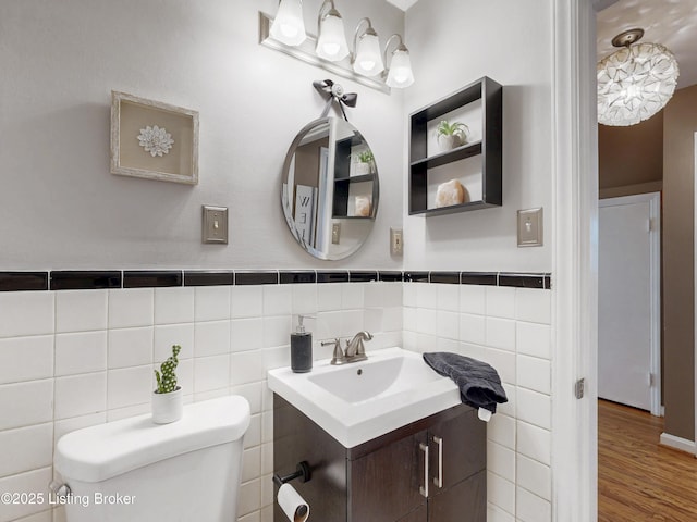 half bathroom featuring tile walls, toilet, wainscoting, vanity, and wood finished floors