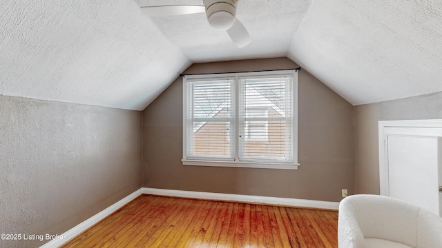 bonus room featuring lofted ceiling, baseboards, a textured ceiling, and light wood finished floors