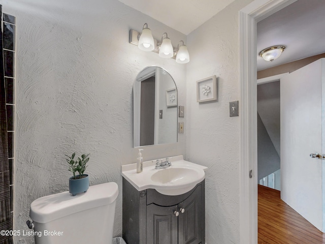 bathroom with a textured wall, wood finished floors, vanity, and toilet