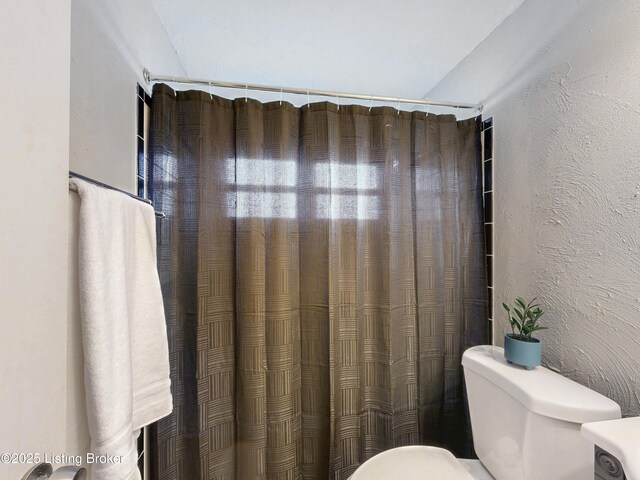 bathroom with curtained shower, a textured wall, and toilet