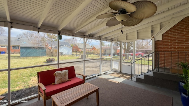 sunroom featuring vaulted ceiling with beams, ceiling fan, and a residential view