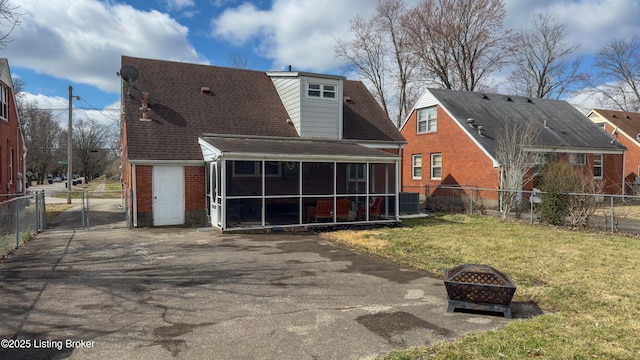 back of property with brick siding, a yard, a sunroom, a gate, and a fire pit