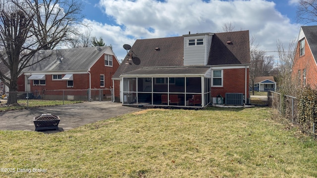 back of property with an outdoor fire pit, a fenced backyard, brick siding, a sunroom, and a yard