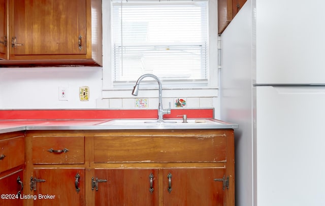 kitchen with light countertops, brown cabinetry, a sink, and freestanding refrigerator