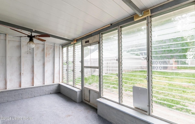 unfurnished sunroom with beamed ceiling, a ceiling fan, and a healthy amount of sunlight