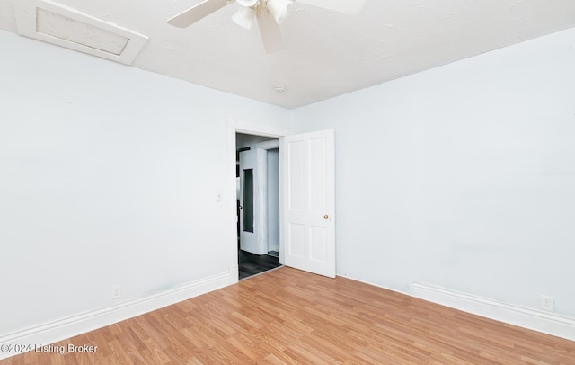 empty room with baseboards, wood finished floors, attic access, and a ceiling fan