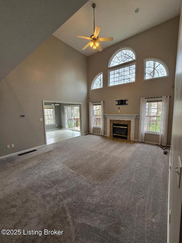 unfurnished living room with visible vents, ceiling fan, a premium fireplace, carpet floors, and high vaulted ceiling