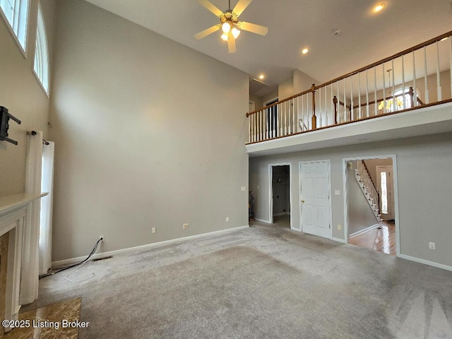 unfurnished living room featuring carpet floors, baseboards, stairway, and a high ceiling