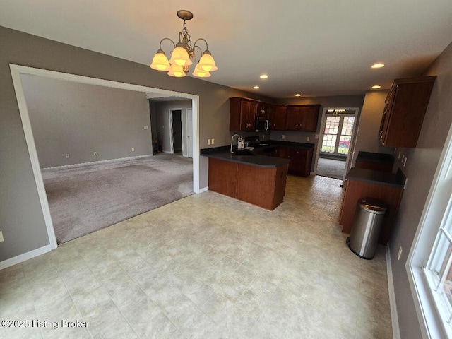 kitchen with light colored carpet, dark countertops, open floor plan, a chandelier, and a sink