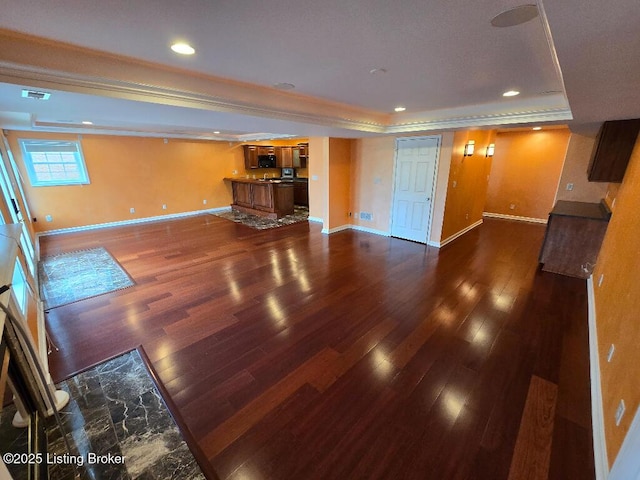 unfurnished living room featuring dark wood-type flooring, a tray ceiling, and baseboards