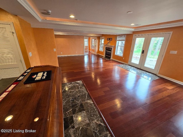 unfurnished living room with wood finished floors, a raised ceiling, crown molding, and french doors