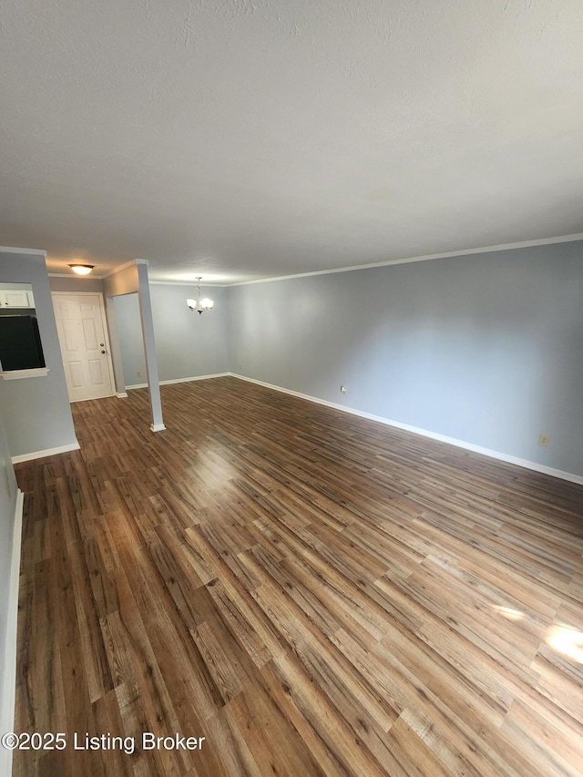 unfurnished living room featuring ornamental molding, wood finished floors, baseboards, and a chandelier