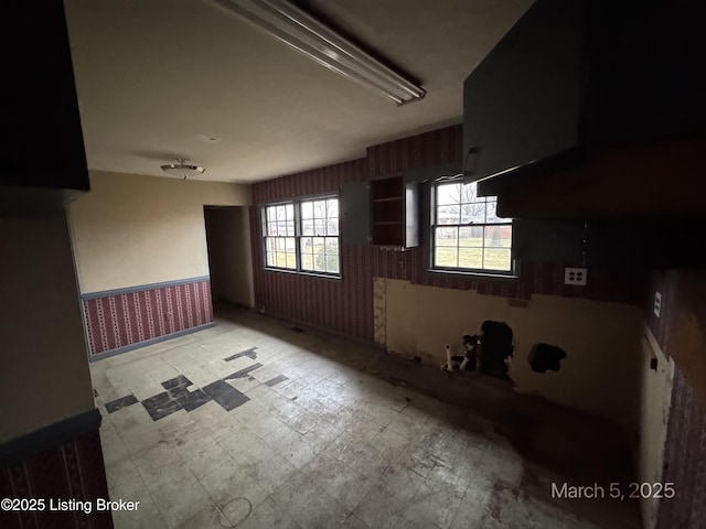 empty room with wallpapered walls, light floors, and wainscoting