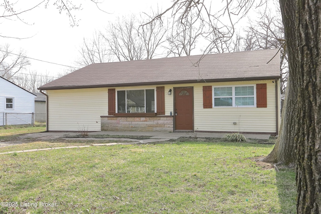 view of front facade with a front lawn, fence, stone siding, and roof with shingles