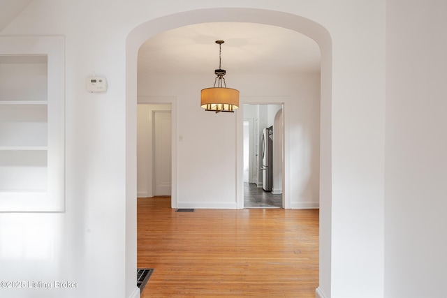 hallway with light wood-style flooring, visible vents, arched walkways, and baseboards