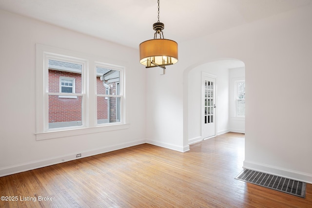 empty room featuring light wood-style flooring, visible vents, arched walkways, and baseboards